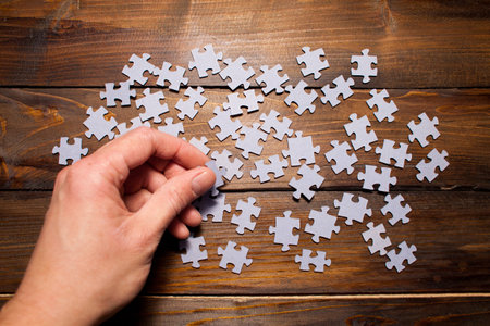 Male hand collects gray puzzle on wooden background. Educational game.