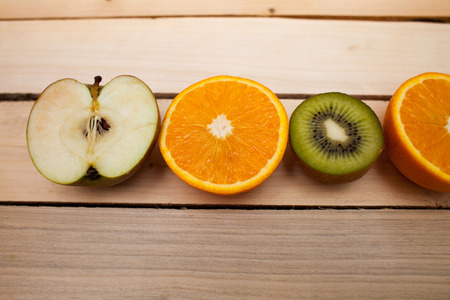 Half-cut green apple, kiwi, orange orange. Juicy fruit on wooden background.の写真素材