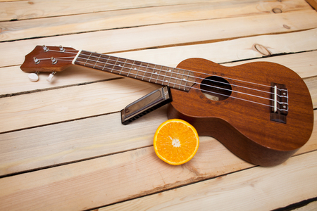 Hawaiian four-stringed ukulele guitar with sliced juicy orange oranges and an iron lip accordion on wooden background.の写真素材
