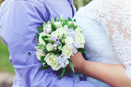 The groom embraces the bride who is holding a bouquet at wedding.
