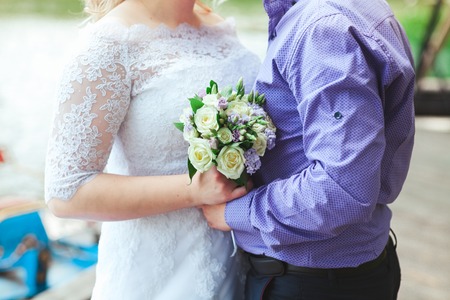 The groom embraces the bride who is holding a bouquet at wedding.の写真素材