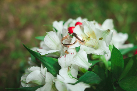 Beautiful golden wedding rings with wedding bouquet of bride on green grass in summer close-up.の写真素材