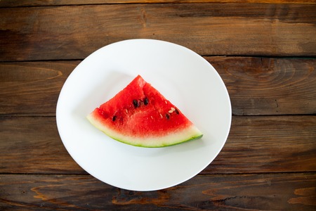 Ripe red watermelon on a wooden background. Slice of watermelon berries in a white plate.の写真素材