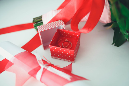Gold wedding rings with a red box on the table with a bouquet of the bride. Red ribbons.の写真素材