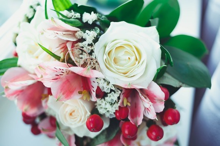 Gold wedding rings on a white table with a bouquet of brides from beautiful flowers.の写真素材