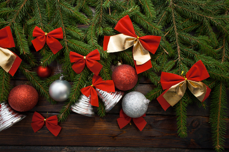 Green living spruce branches on a dark wooden background. New Year background with beautiful balls and red bows and bells. Top view.の写真素材