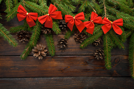Green living spruce branches on a dark wooden background. New Year background with cones and red bows. Top view.の写真素材