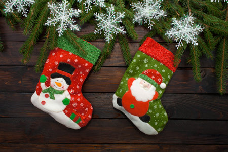 Green Christmas tree branches on a dark wooden background. New Year background with socks and white snowflakes. Top view.の写真素材