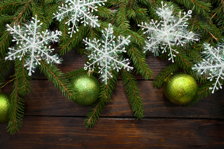 Green living spruce branches on a dark wooden background. New Year background with green balls and white snowflakes. Top view.の写真素材