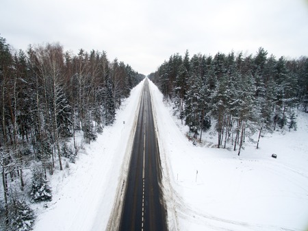 Winter forest and asphalt road. View from above. The photo was taken with a drone. Pine and spruce forest with a black road in the snow.の写真素材