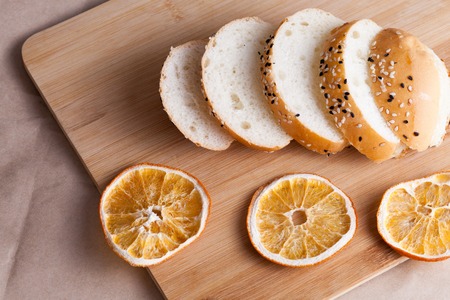 Hot sweet buns cut into pieces on a rustic background. Shaped food with sesame on cutting board and dry oranges.の写真素材