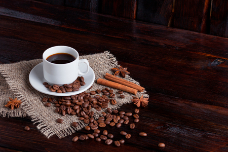 White cup of coffee with coffee grains near on linen fabric on the dark vintage background.の写真素材