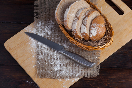 Fresh brown bread with sliced pieces on an oak board with scattered flour on a wooden background with of linen fabric with a steel knife. Photo top viewの写真素材