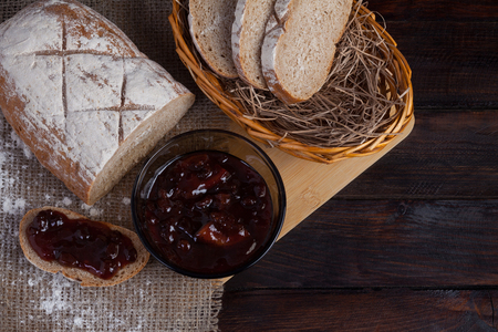 Freshly sliced pieces bread in a wicker bowl on an oak board with scattered flour on a wooden background with of linen fabric next to a bowl of a delicious jamの写真素材
