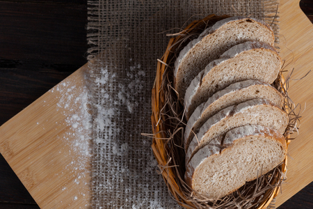 Freshly sliced pieces in a wicker bowl on an oak board with scattered flour on a wooden background with of linen fabric. Photo top view.の写真素材