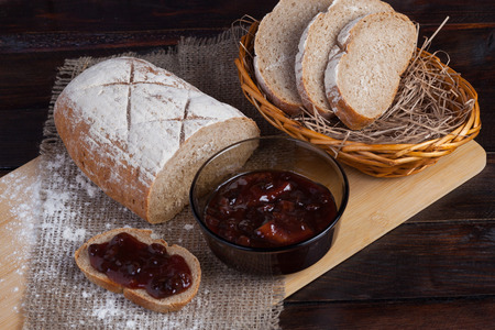 Freshly sliced pieces bread in a wicker bowl on an oak board with scattered flour on a wooden background with of linen fabric next to a bowl of a delicious jamの写真素材