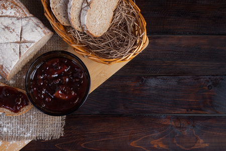 Freshly sliced pieces bread in a wicker bowl on an oak board with scattered flour on a wooden background with of linen fabric next to a bowl of a delicious jamの写真素材
