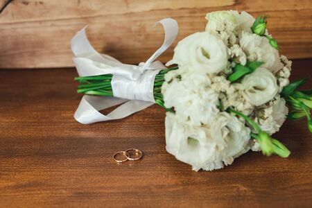 Wedding rings with a beautiful bridal bouquet on a wooden background.の写真素材