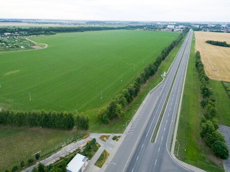 Top view asphalt road, highway, a crossroads in the village on a bright sunny day. Aerial photo with green forest, grassの写真素材