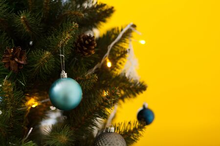 Beautiful green Christmas tree decorated with balls and garlands. Close-up photo. Yellow backgroundの写真素材