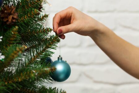 Female hand hangs a beautiful blue ball on a merry Christmas tree. Close-up photoの写真素材