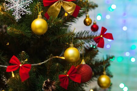 Beautiful green Christmas tree decorated with yellow balls, red bows and garlands. Close-up photo. Sparkling backgroundの写真素材