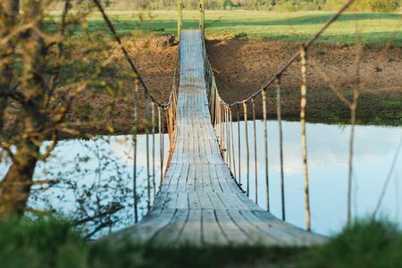 Old suspended wooden foot bridge over the river. Photo on a summer day. River crossing for peopleの写真素材