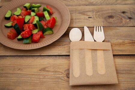 paper cardboard dishes with vegetable salad tomatoes cucumbers with wooden devices fork knife horseの写真素材