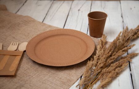 ecological disposable tableware paper cardboard empty on a wooden white table with yellow flowersの写真素材