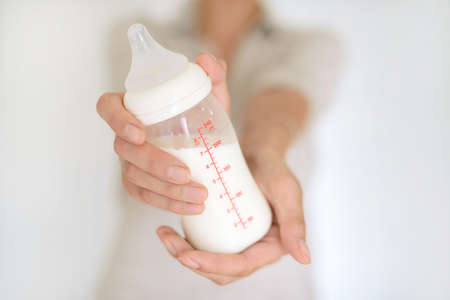 Woman hand holding a baby bottle of milk over blurred backgroundの写真素材