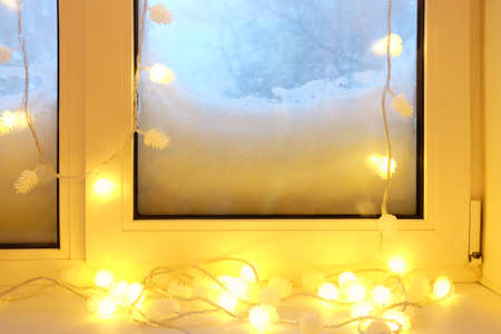 Electric garland on the windowsill at snowy winter eveningの写真素材