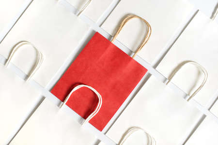 One red shopping bag in background of white bags isolated on white background. Black friday or Christmas sales.の写真素材