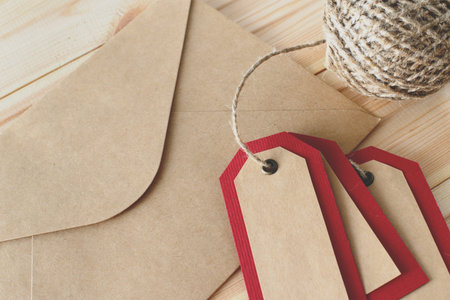 Recycled craft paper envelope and red tags on vintage wooden table background. Top view. Mock up sample.の写真素材