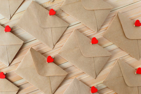 Envelopes from craft paper with red heart pins on the wooden background.の写真素材