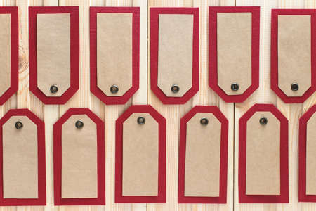 Recycled craft paper red tags in a row on vintage wooden table background. Top view. Mock up sample.の写真素材