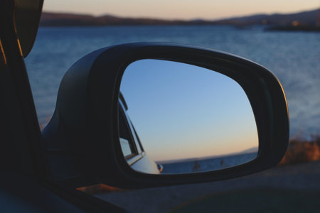Reflection of the sunset in the sea in a car side view mirror.の写真素材