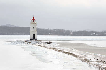 Red and white lighthouse at winter snowy sea coast. Free copy space.の写真素材
