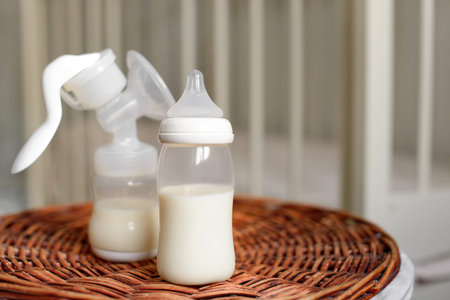 Breast pump and bottle with milk for baby on a straw basket. Kids room with a bed.