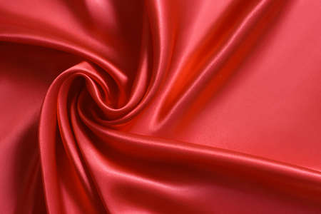 Close up of ripplesin shape of rose flower in red silk fabric. Satin textile background.の写真素材