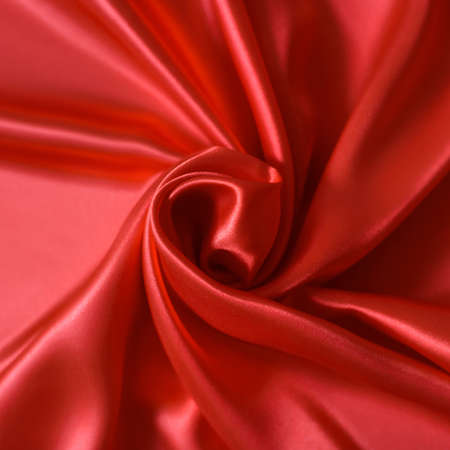 Close up of ripplesin shape of rose flower in red silk fabric. Satin textile background.の写真素材