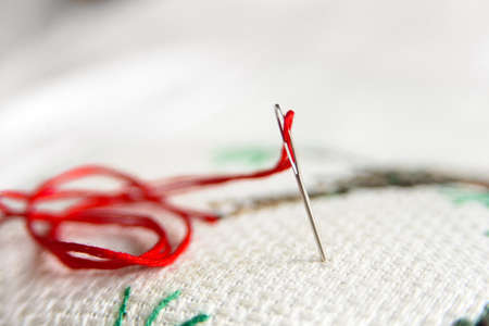 Cross-stitch embroidery and needle with red thread. Embroidery macro close up. View from above. Free copy space.の写真素材