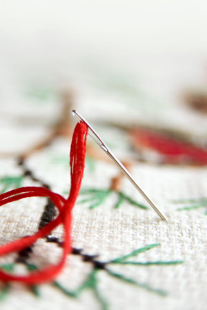 Cross-stitch embroidery and needle with red thread. Embroidery macro close up. View from above. Free...