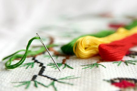 Cross-stitch embroidery and needle with red thread. Embroidery macro close up. View from above. Free copy space.の写真素材