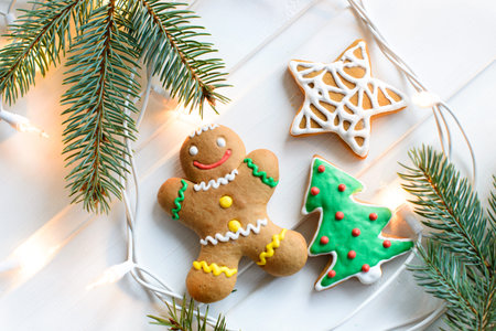 Christmas cookies with festive decoration and christmas lights on white wooden background.