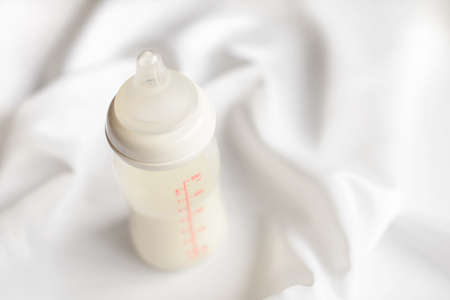 Bottle of milk for newborn baby over white silk satin background. Free copy space. Maternity and baby care concept.の写真素材