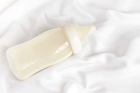 Bottle of milk for newborn baby over white silk satin background. Free copy space. Top view. Maternity and baby care concept.の写真素材