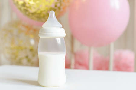 Baby bottles with breast milk with various festive paper decor and balloons in front of baby bedroom. It's a girl or baby birthday celebration concept. Baby shower concept.の写真素材