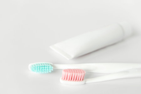 Close up of two plastic white toothbrushes with pink and blue bristle and toothpaste in tube on white background.の写真素材