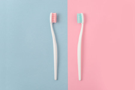 Close up of two plastic white toothbrushes with pink and blue bristle on pink and blue background. Free copy space.の写真素材