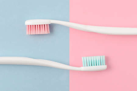 Close up of two plastic white toothbrushes with pink and blue bristle on pink and blue background. Free copy space.の写真素材